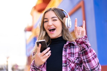 Young pretty Romanian woman at outdoors listening music with a mobile making rock gesture