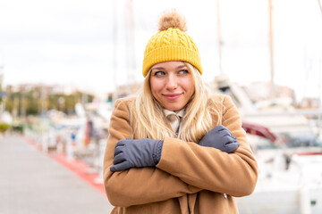 Young pretty blonde woman wearing winter jacket at outdoors freezing