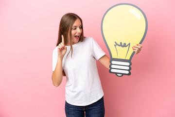 Young Lithuanian woman isolated on pink background holding a bulb icon and thinking