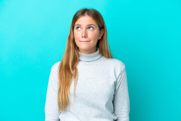 Young blonde woman isolated on blue background having doubts while looking up