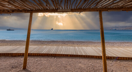 Coastal landscape of the Red Sea with wooden frame of sunshade and pedestrian walkway for vacationers, tropical winter weather just befor