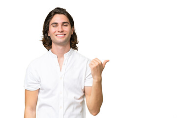 Young caucasian man isolated on green chroma background pointing to the side to present a product