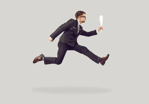 Busy office worker hurrying to work. Company employee is late for work meeting. Profile view of funny young man in suit and glasses running with some documents and business report in hand