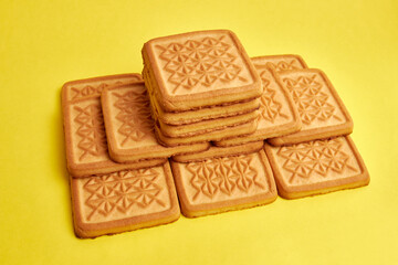 A pile of square cookies on a yellow background. A tasty and sweet snack.