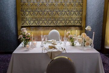 Banquet table decorated with plates, cutlery, candles, glasses and flower arrangements