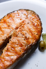 Delicious salmon fish steak cooked on grill and served on white ceramic plate in a sea food restaurant
