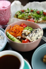 Poke bowl with healthy and natural ingredients served in a restaurant. Exotic lunch meal prepared with hummus dip, sliced avocado, cucumbers, Korean carrot and black sesame seeds