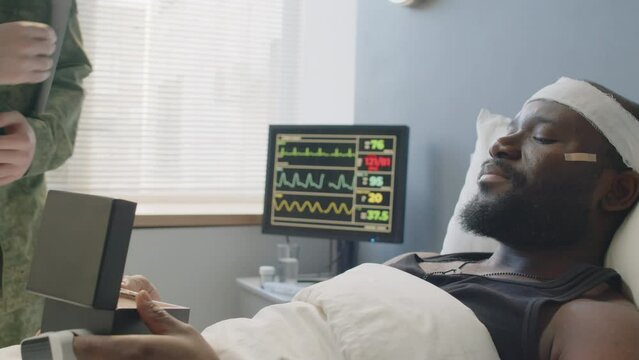 African American lieutenant with head injury lying in hospital bed receiving medal as military award for heroism