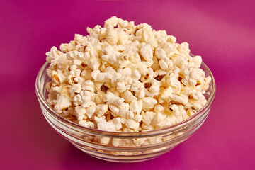A bowl on a pink background is completely filled with popcorn. A sweet snack.