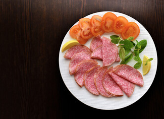 Salami with sliced tomatoes, mint and lemon on a white plate.  Copy space is on the left side.  Flat lay top view photo.  Food from above. 