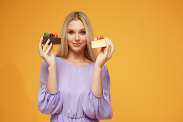 Beautiful blonde girl in a lilac dress with cakes on a yellow background. Studio. Diet and health