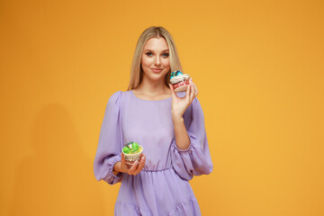 Beautiful blonde girl in a lilac dress with cakes on a yellow background. Studio. Diet and health