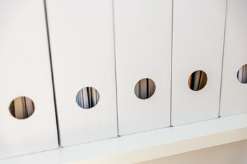 White-colored binders lined up in a row on a shelf in a minimalist arrangement.  
cardboard binders...