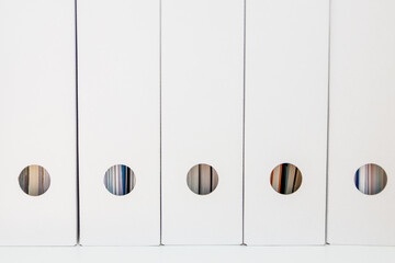 White-colored binders lined up in a row on a shelf in a minimalist arrangement.  
cardboard binders ecology concept in the office 