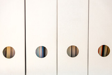 White-colored binders lined up in a row on a shelf in a minimalist arrangement.  
cardboard binders...