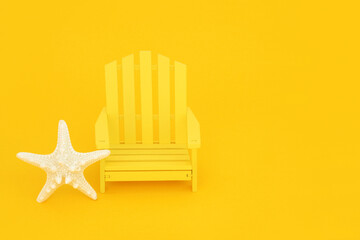 Down at the beach minimal summer holiday concept with yellow wooden slatted chair, starfish seashell on yellow background. Solitary, alone, relaxation, travel, nature concept composition. Copy space.
