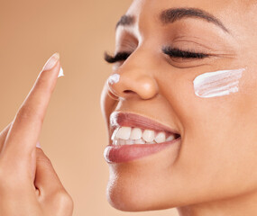 Face, skincare smile and woman with cream in studio isolated on a brown background. Dermatology, beauty cosmetics and closeup of happy female model with lotion, creme or moisturizer for skin health.