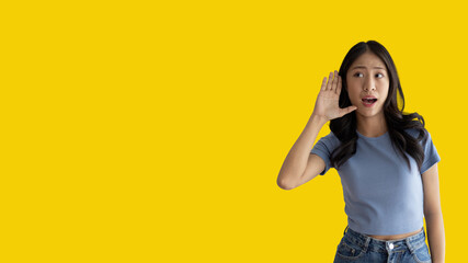 Asian woman eavesdropping or overhearing secret conversation isolated on yellow background, Gossip,...