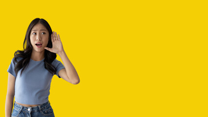 Asian woman eavesdropping or overhearing secret conversation isolated on yellow background, Gossip,...