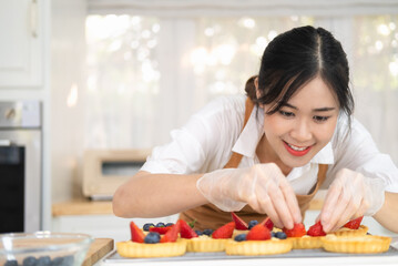 Happy young housewife hands in cooking gloves decorating freshly baked tart with blueberries strawberry fresh fruit.Woman chef baker wear apron making fruit tart. homemade bakery at home.