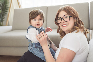 cute funny lady wear white t-shirt smiling and playing with baby girl inside the living room