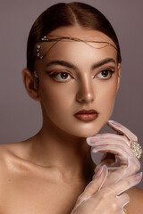 Female model with red hair, brown eyes, freckled skin, poses for a beauty shoot. Model wears a white mesh glove and pearl ring, holding her hand to her face.  Brown background.