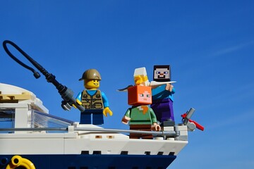 Fototapeta premium LEGO Minecraft Steve and Alex on yacht with a boy with fishing pole from LEGO Creator series, enjoying sunny day on sea. Seagull is visible in hands of smiling Steve. 