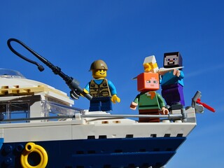 Fototapeta premium LEGO Minecraft Steve and Alex on yacht with a boy with fishing pole from LEGO Creator series, enjoying sunny day on sea. Seagull is captured in hands of smiling Steve. 