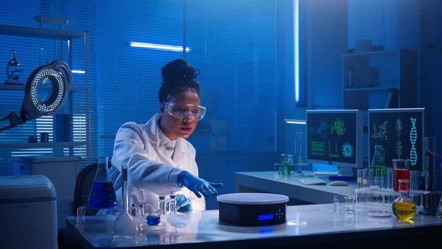 An African American woman examines virtual graphics, zoomes the picture. Black female doctor or researcher works in biochemical modern laboratory with blue light.