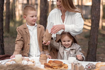 Family with children enjoying an Easter picnic in a spring garden. Mom and kids having fun outdoor lunch in spring forest, eating bread, pancakes, eggs and drinking milk in rustic style