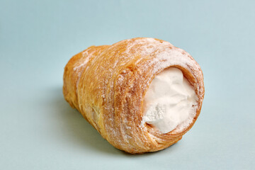 Pipe of puff pastry with meringue on a blue background.