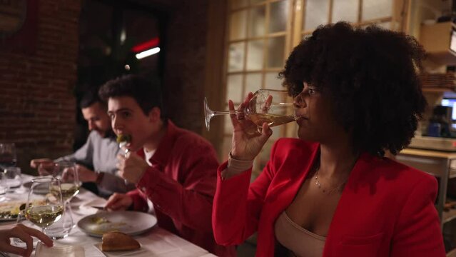 group of people having dinner in restaurant - focus on african american woman drinking white wine -