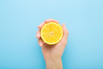 Young adult woman hand holding one half of yellow lemon. Fresh fruit. Light blue table background....