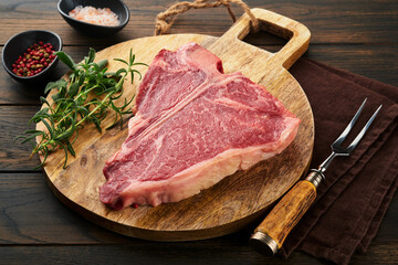 Thick Raw T-Bone Steak. Dry-aged Raw T-bone or porterhouse beef meat Steak with herbs and salt on dark background. Selective focus and copy space.
