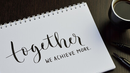 TOGETHER WE ACHIEVE MORE black hand lettering in notebook with cup of espresso and pens on black...