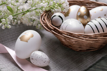 Many painted Easter eggs, branch with lilac flowers and ribbon on table
