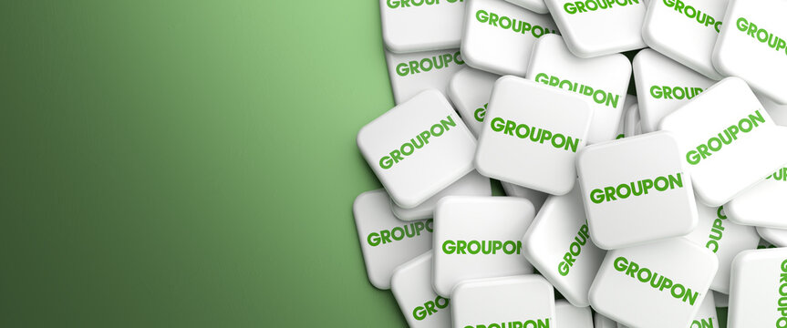 Logos of the e-commerce marketplace Groupon on a heap on a table. Copy space. Web banner format.