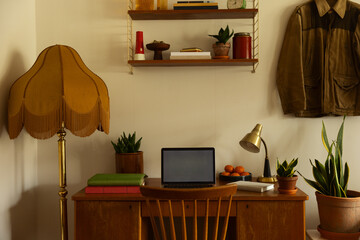 A home office wooden desk in a living room filled with lamps, plants, books and other decorations with a retro look. 