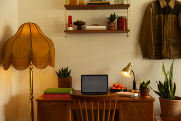 A home office wooden desk in a living room filled with lamps, plants, books and other decorations with a retro look. 