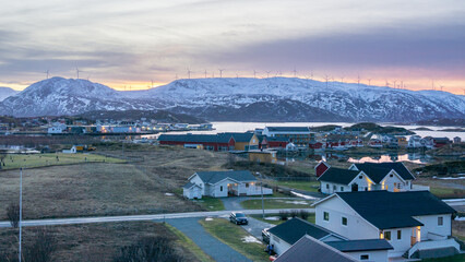 Sonnenaufgang mit Morgenrot über der Insel Kvaløya mit Windrädern und dem Dorf Sommarøy im Vordergrund. bunte Häuser am Ufer des Atlantik in Norwegen bei Tromsø