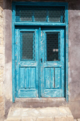 Access to a house with an old weathered and petrol painted double wooden door.