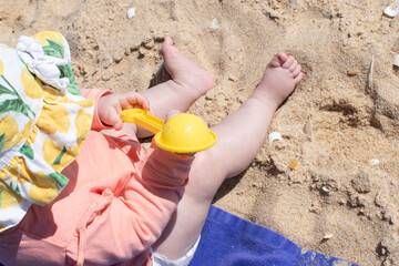 Unidentifiable baby girl playing in the sand with plastic toy in her hands. Child playing in the sand on holiday at the beach. Select focus.