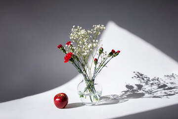 A bouquet of flowers and a red apple. Light and shadow. Flowers of red carnation and white...