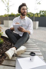 Fototapeta premium Man writing in notepad while sitting on bench with legs