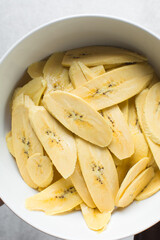 slices of ripe plantains in a white bowl, slices of yellow plantains for frying, process for making fried plantain