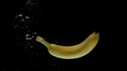 Slow motion one banana falling into transparent water on black background. Fresh fruits splashing in aquarium. Healthy food, diet, air bubbles - Powered by Adobe