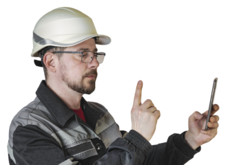 Positive friendly bearded male builder in overalls, safety helmet and goggles looks at the phone and shows hand gesture. Isolated background.