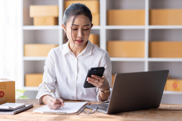 Fototapeta premium Portrait of Starting Asian female small businesses owners SME entrepreneur working at Laptop in home Warehouse, online marketing, packing boxes, SME sellers, concept, e-commerce team, online sales.