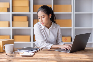 Fototapeta premium Portrait of Starting Asian female small businesses owners SME entrepreneur working at Laptop in home Warehouse, online marketing, packing boxes, SME sellers, concept, e-commerce team, online sales.