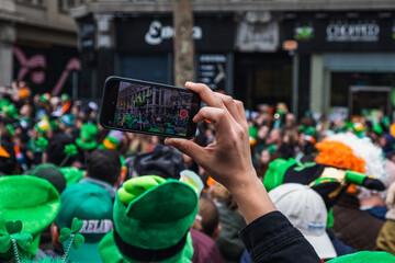 Hand with phone, taking picture of the parade green costume and green hats, people, Paddy's day Dublin centre, Ireland